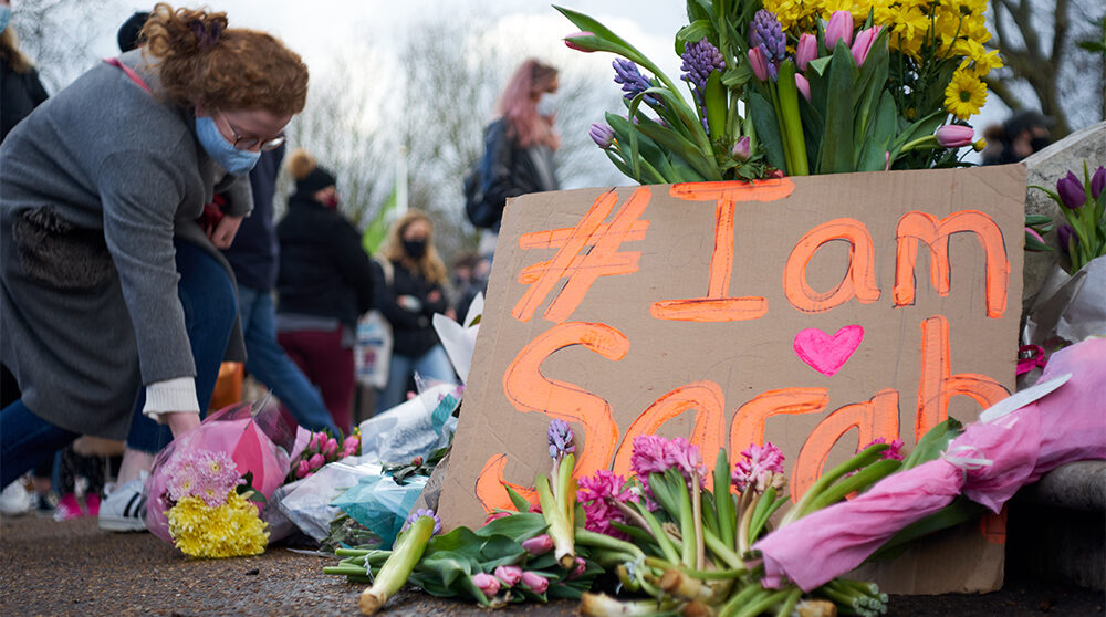 En kvinna lägger blommor vid en minnesmanifestation för Sarah Everard i Storbritannien.