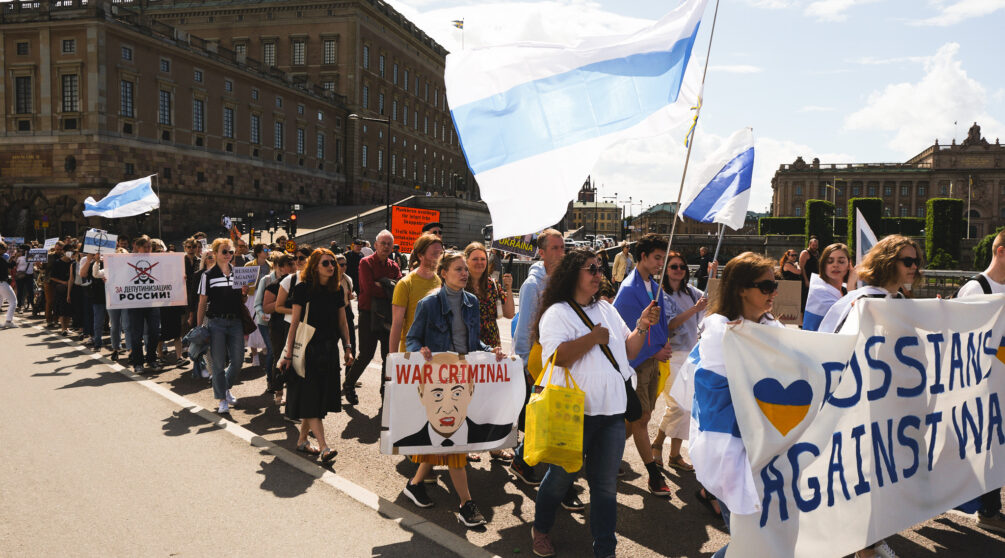 Människor demonstrerar mot kriget i Ukraina med flaggor och banderoller.