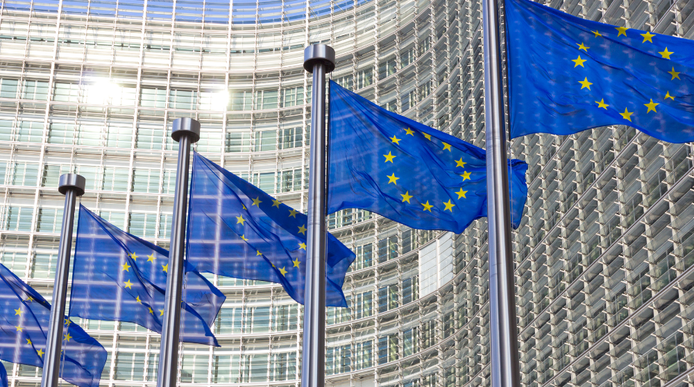 Några EU-flaggor vajar i vinden framför en EU-byggnad.